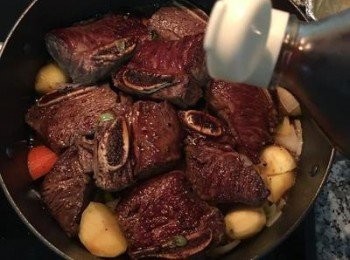 step8: 將牛小排鋪平在蔬果上面；倒入壽喜燒醬汁與米酒，大火煮滾；