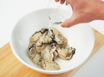 step3: 將牡蠣移至乾淨的盆中，淋上1大匙酒清洗，接著倒入篩網瀝乾水分。