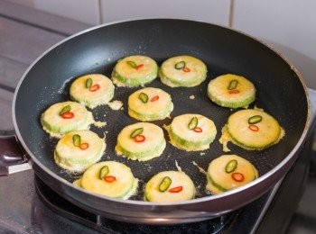 step7: 以小火燒熱鍋子，下少許油並待至油熱後，把翠玉瓜沾上蛋液後下鍋，盡快下夠要煎的份量。趁表面的蛋液未凝固放上辣椒圈。調至中小火多煎約 3 分鐘至底部金黃色。