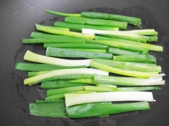 step4: 在平底鍋中開小火倒入適量的油，把對半切的蔥鋪平。