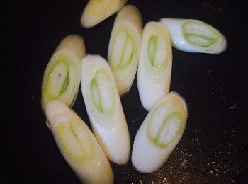 step2: 京葱斜切成厚片。燒熱鑊，用剛才煎雞皮剩下的油將京葱煎至微焦，盛起備用。焦糖化後的京葱味道會比較甜。