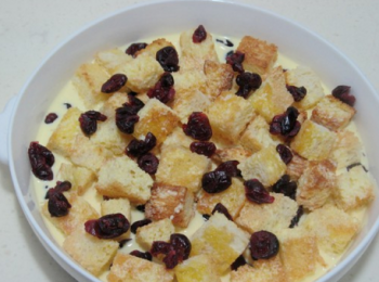 step9: 黃油隔水融化後，將烤好的吐司丁蘸上薄薄的黃油液後，放在烤盤中，然後倒入布丁液，最上面再撒一些蔓越莓幹。