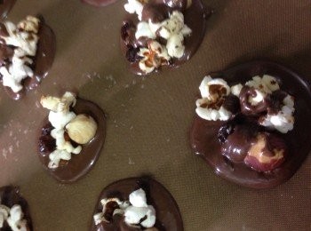 step2: 用，用匙羹底部沾朱古力漿並抹在烘焙紙上成圓形狀並加上爆谷,提子乾，牛奶糖及榛子