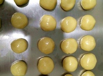 step4: 取一個餅皮小球，壓扁成比較大比較扁的圓形，加入蓮蓉小球壓扁，包入2個咸鴨蛋蛋黃，蛋黃在中間，手指向里推，直至全包住餡料，包好的月餅，丟到麵粉里，滾上一層薄薄的麵粉，拿起放入月餅模具，壓平