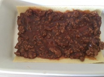 step6: 準備千層麵皮：燒一鍋水，水裡放少量鹽燒開，放入千層面，按包裝袋上標示的時間煮好，撈出放入裝滿冰水的盆中冷卻。接著烤盤刷上一層薄薄的油，麵皮放入烤盤底部，鋪上肉醬。