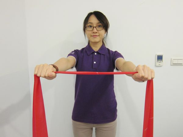 動作1：肩膀自然下垂，手臂往前打直，手握彈力帶（或用絲襪替代）與肩同寬，高度於胸前，做預備動作。